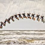 Een compositiefoto toont een persoon die kiteboardt, vastgelegd in meerdere beelden terwijl hij hoog boven de woeste oceaangolven springt en een boog vormt door de bewolkte lucht.