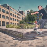 Een persoon met kort haar skateboardt op een houten richel bij een fontein op een stedelijk plein, omgeven door bakstenen en glazen gebouwen onder een heldere hemel. Een andere persoon staat bij de fontein op de achtergrond.
