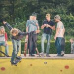 Een groep jongeren met skateboards verzamelt zich buiten bij een gele skatebaan. Eén persoon is actief aan het skateboarden terwijl anderen toekijken, kletsen of in de buurt zitten. Bomen en groen zijn zichtbaar op de achtergrond.