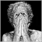 Zwart-wit portret van een oudere persoon met krullend haar, met de handen over de mond en neus, de ogen wijd open, met een expressief gezicht tegen een effen zwarte achtergrond.