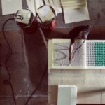 Een persoon werkt met schuimvulling op een werktafel, schikt of monteert veren. Twee cilindrische containers en schuimvellen staan vlakbij in de industriële werkruimte, van bovenaf gezien.